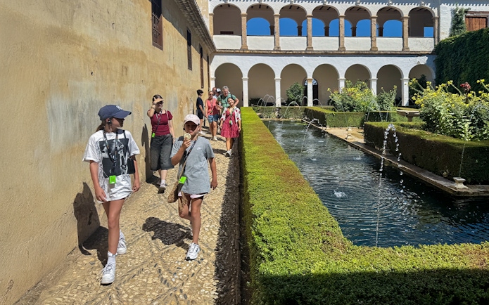 Tourists walking with guide at Alhambra courtyard, Granada, Spain.