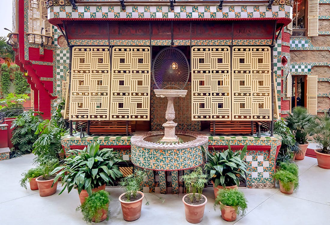 Casa Vicens backyard with vibrant mosaic tiles and lush greenery in Barcelona, Spain.