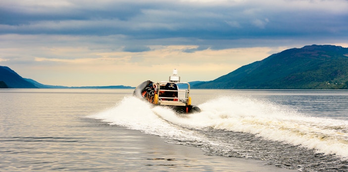 Speedboat cruising on Loch Ness with scenic hills in the background.