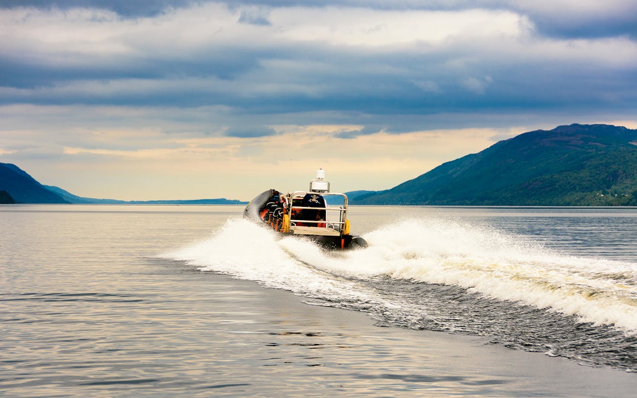 Speedboat cruising on Loch Ness with scenic hills in the background.