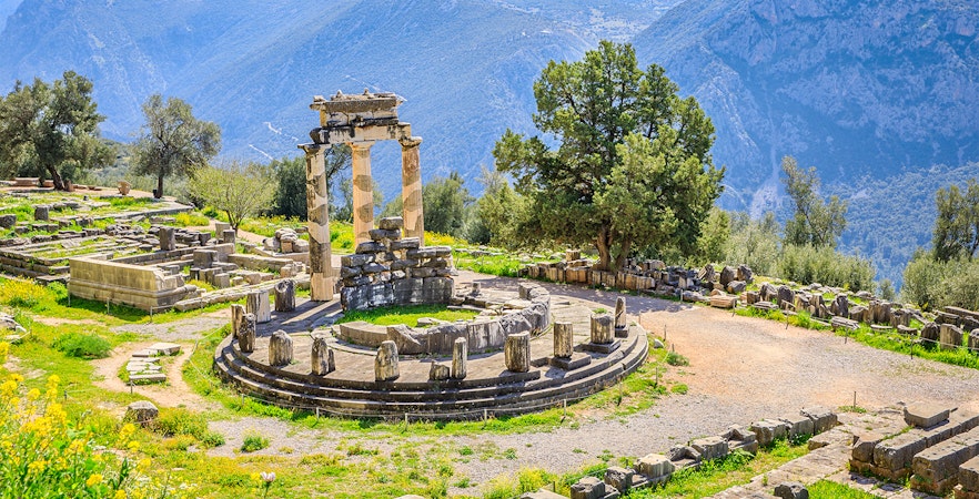 Ancient ruins of the Tholos of Delphi with mountains in the background, Greece.