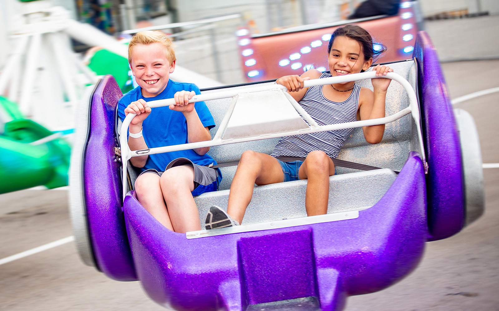 Two diverse kids riding an amusement park ride at the fun theme park.