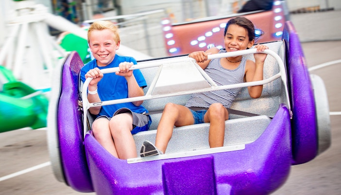 Two diverse kids riding an amusement park ride at the fun theme park.