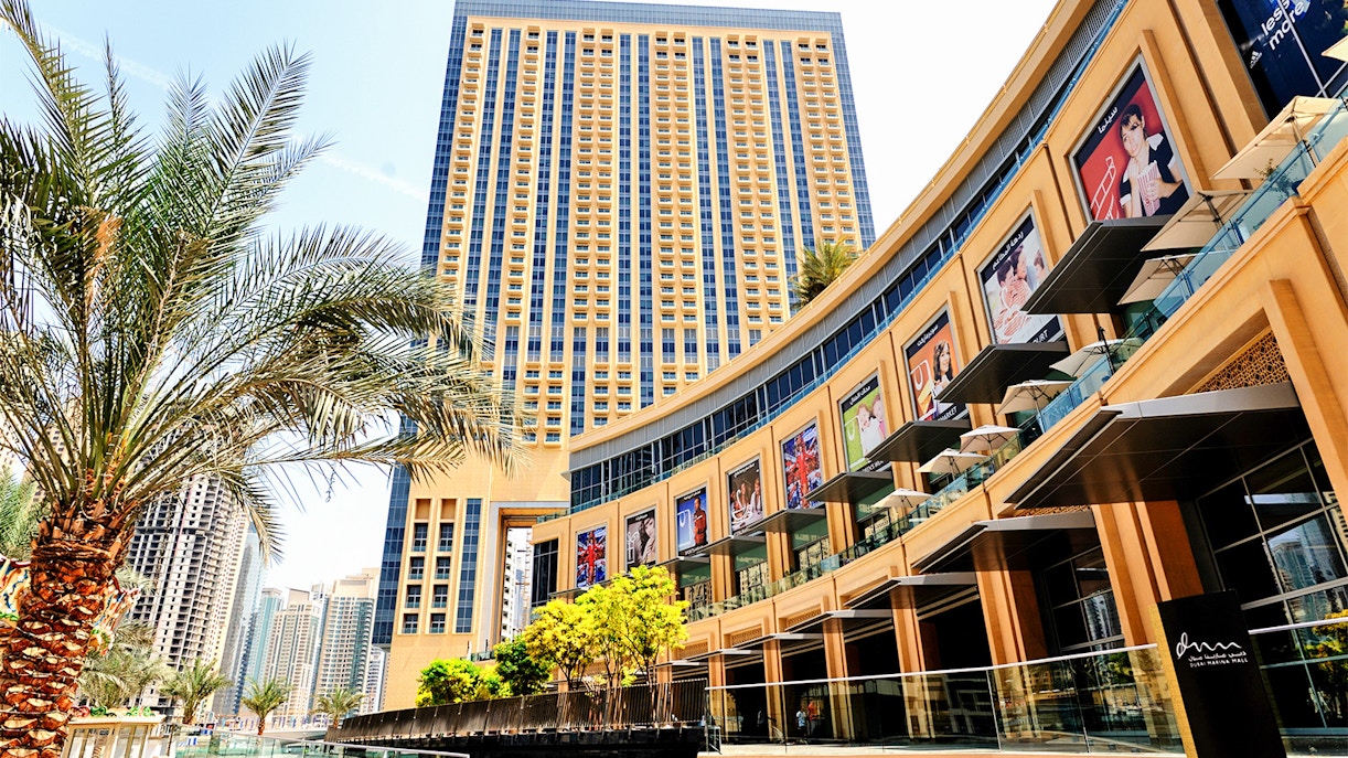 Dubai Mall exterior with palm trees and high-rise buildings in the background.