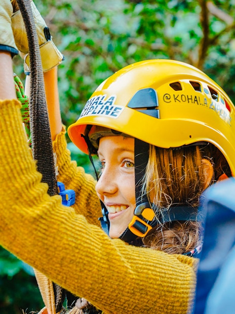 Guest zip lining on Kohala Canopy Adventure, wearing a helmet and harness.