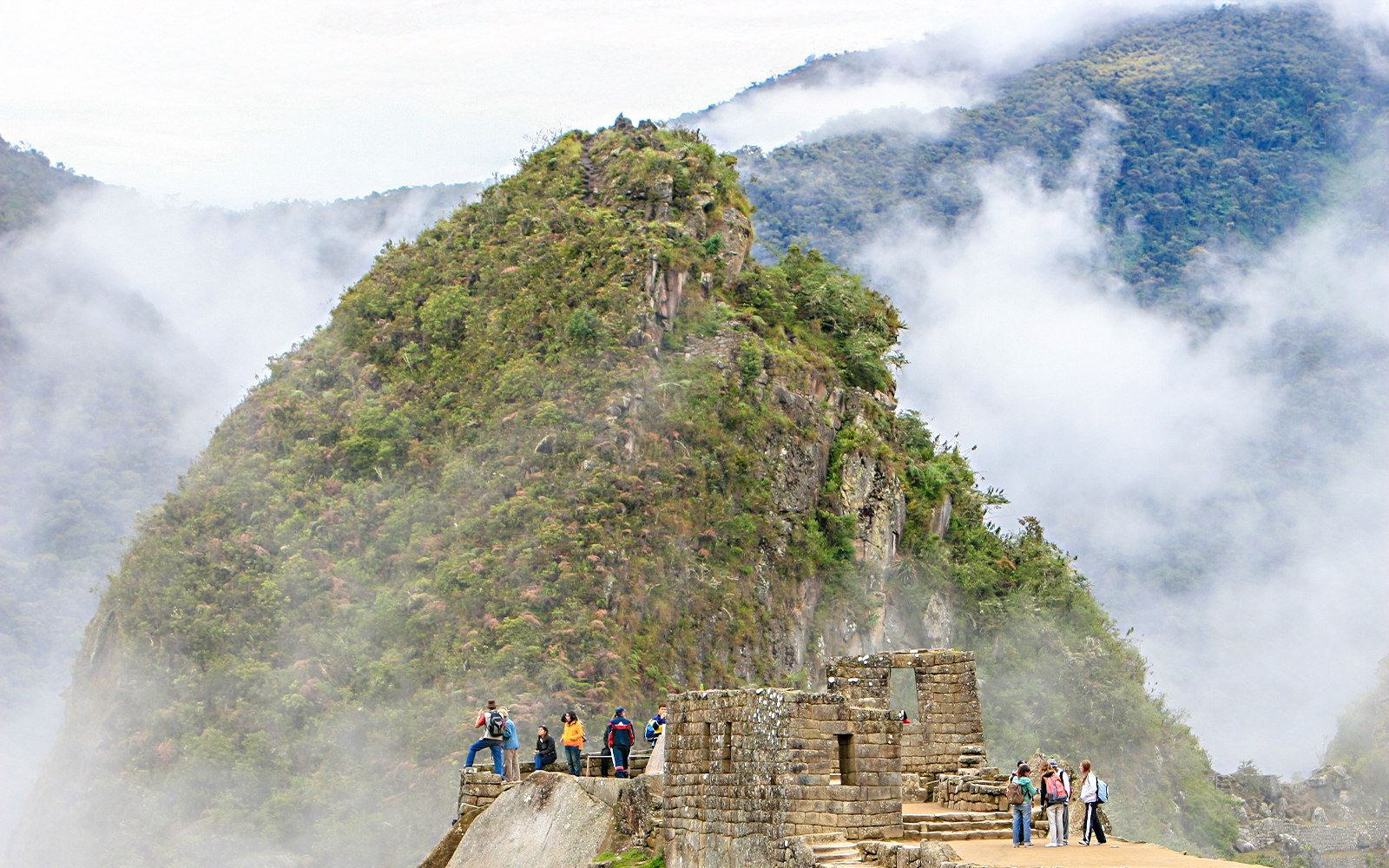 Hikers exploring Huchuy Picchu with misty mountain backdrop at Machu Picchu, Peru.