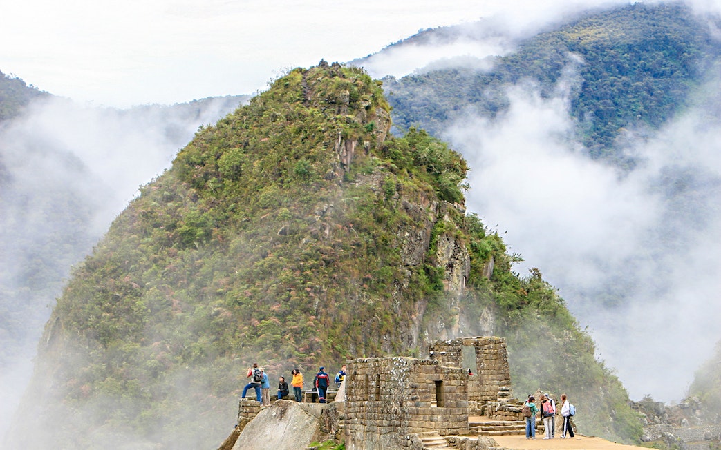 Hikers exploring Huchuy Picchu with misty mountain backdrop at Machu Picchu, Peru.