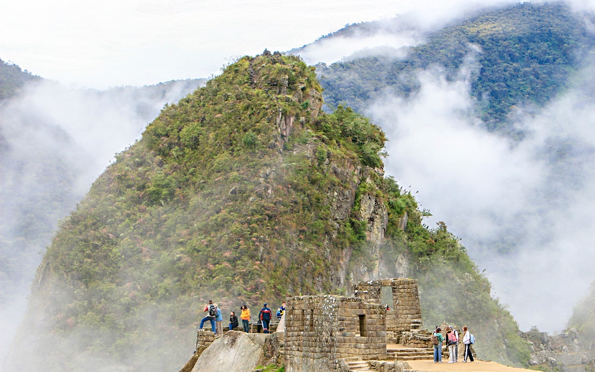 Hikers exploring Huchuy Picchu with misty mountain backdrop at Machu Picchu, Peru.