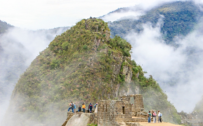 Hikers exploring Huchuy Picchu with misty mountain backdrop at Machu Picchu, Peru.