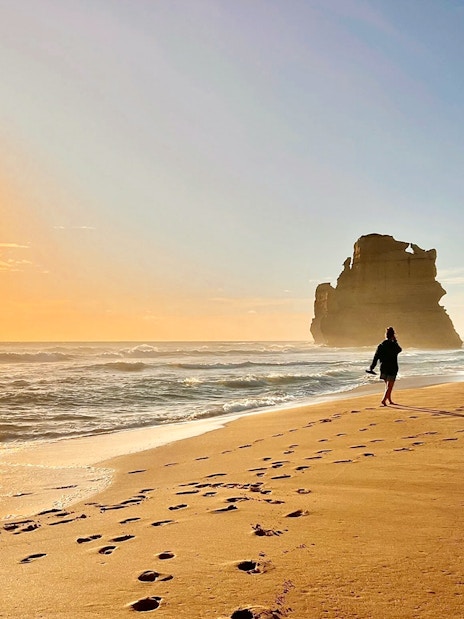 People walking on a beach at sunset near rock formations on the Great Ocean Road.