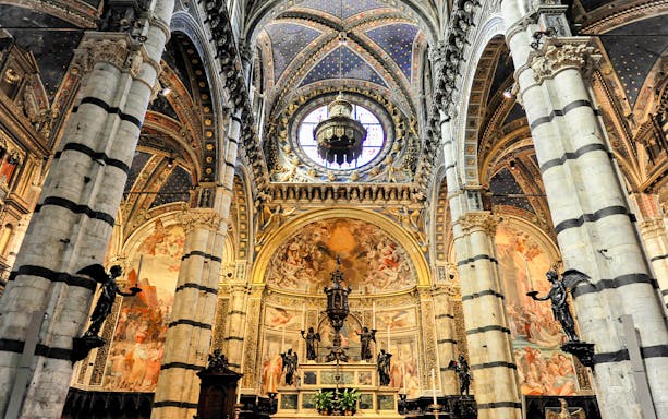 Siena Duomo interior with ornate frescoes and striped columns.