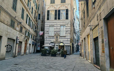 Narrow cobblestone street in Genoa with historic buildings and a small café, part of the city exploration game.