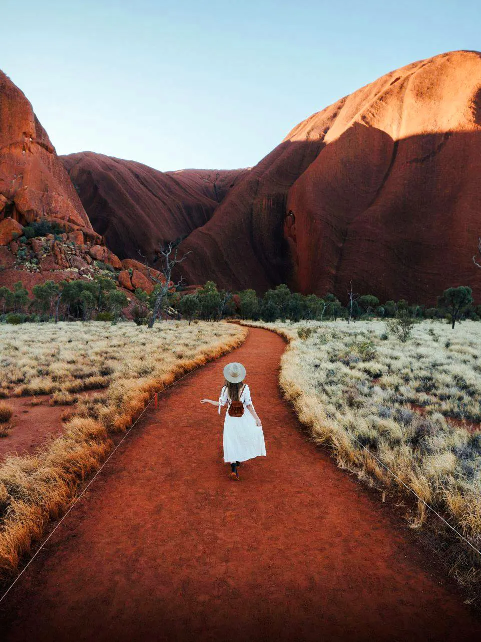 Tourist walking along a red dirt path in Uluru-Kata Tjuṯa National Park, Australia.