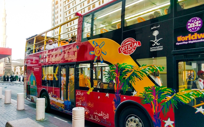 Red double-decker bus on Al Madinah Hop-On Hop-Off Tour with passengers on board.