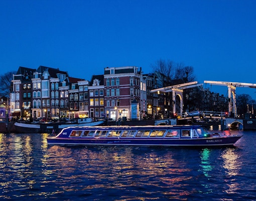 Amsterdam evening canal cruise with illuminated bridges and historic buildings.