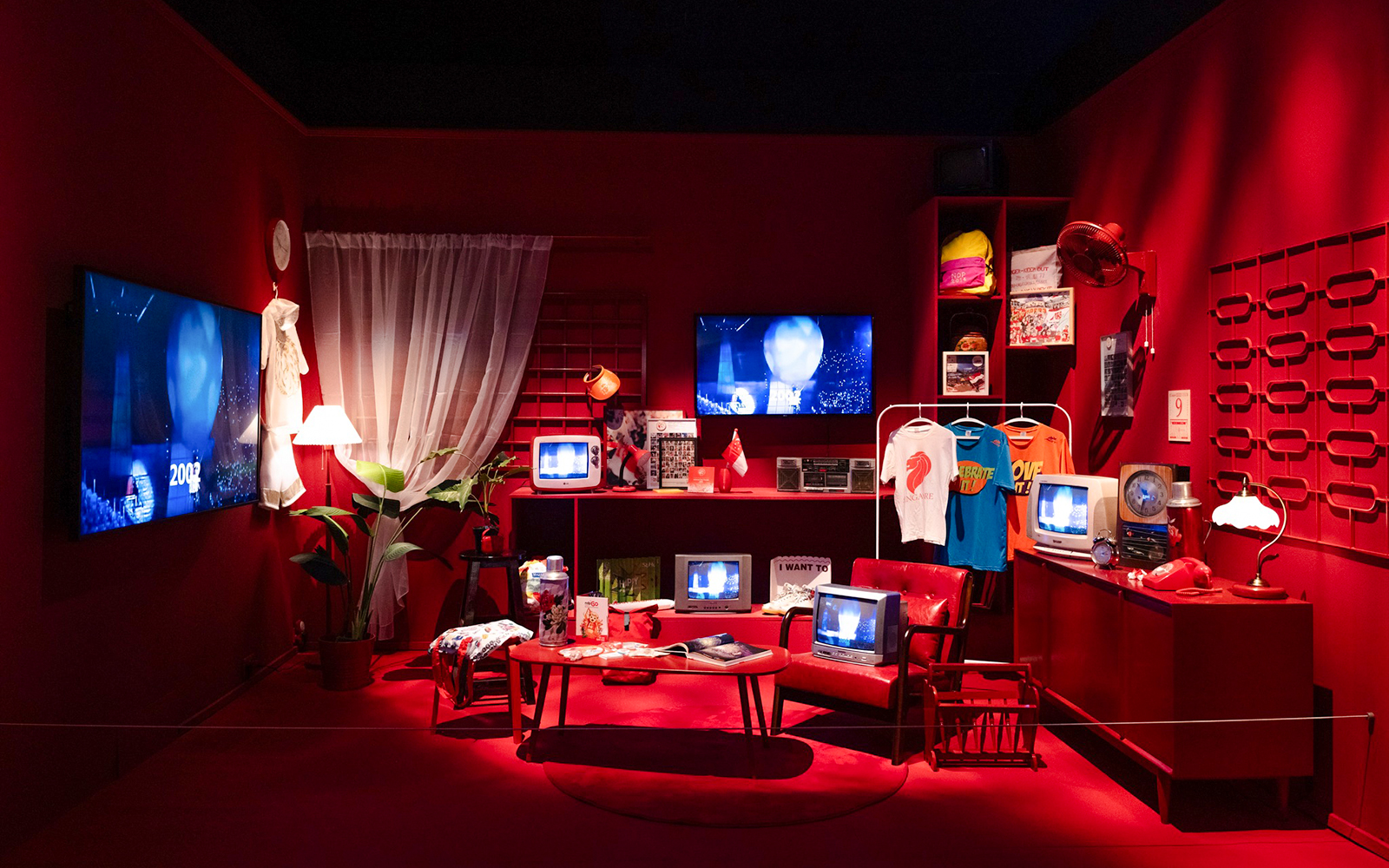 Red room with vintage televisions, clothing, and cultural artifacts on display.