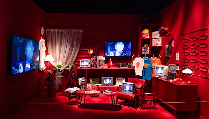 Red room with vintage televisions, clothing, and cultural artifacts on display.