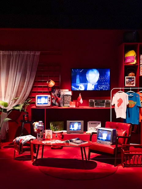Red room with vintage televisions, clothing, and cultural artifacts on display.