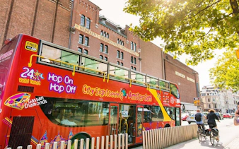 City Sightseeing Amsterdam bus near Heineken Brewery with cyclists nearby.