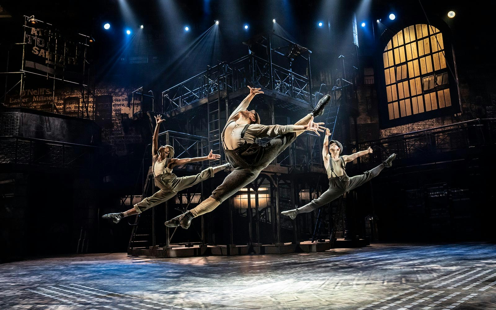 Performers leaping on stage during Newsies West End show.