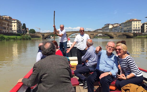 Guided boat tour on a Florentine gondola with tourists enjoying the Arno River view.