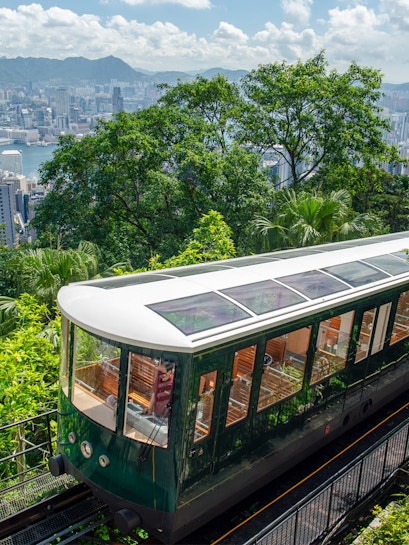 Hong Kong Peak Tram ascending with city skyline and greenery in the background.