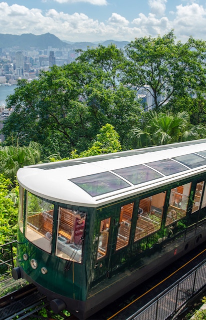 Hong Kong Peak Tram ascending with city skyline and greenery in the background.