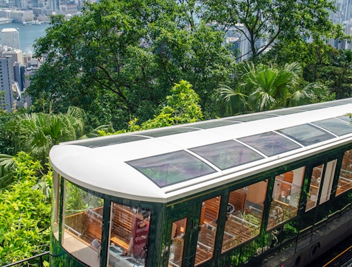 Hong Kong Peak Tram ascending with city skyline and greenery in the background.