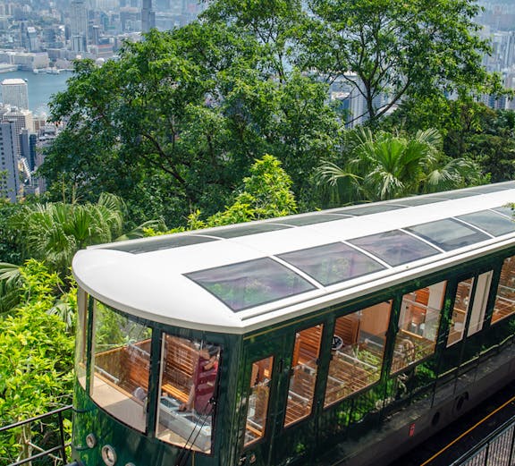 Hong Kong Peak Tram ascending with city skyline and greenery in the background.
