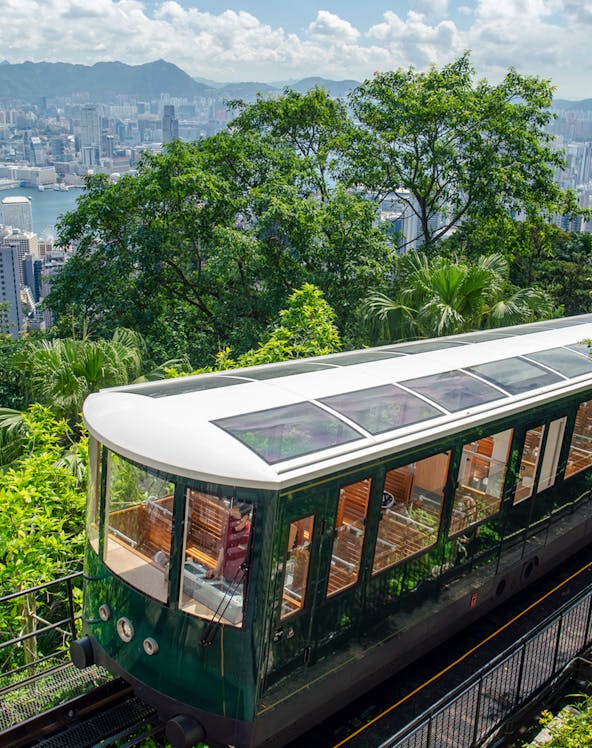 Hong Kong Peak Tram ascending with city skyline and greenery in the background.