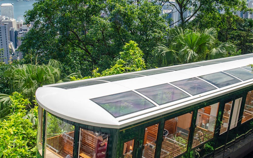 Hong Kong Peak Tram ascending with city skyline and greenery in the background.