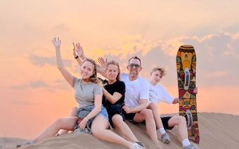 Group enjoying sunset on Abu Dhabi desert safari with sandboard.