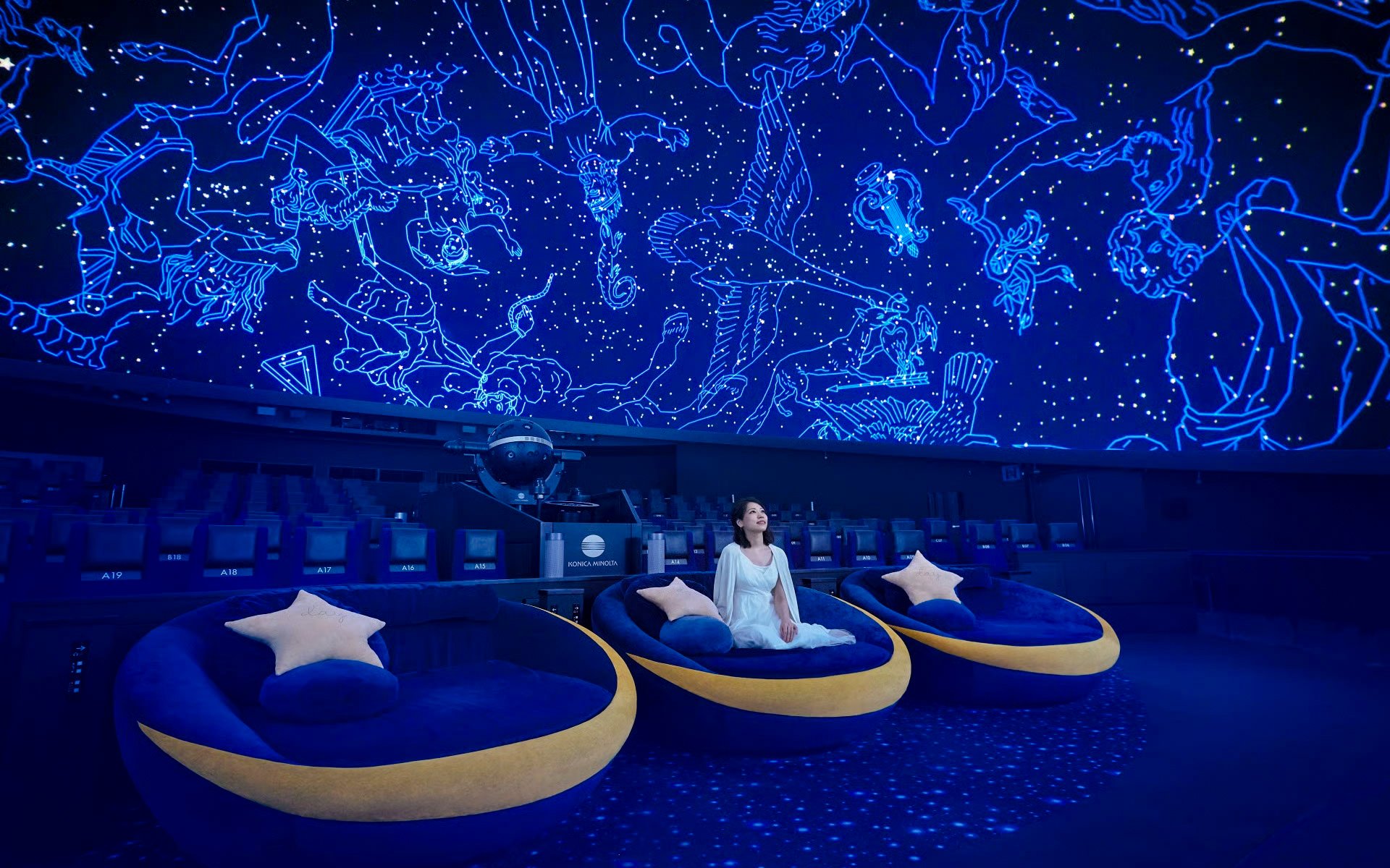 Tourists seated under a starry sky projection at a planetarium.