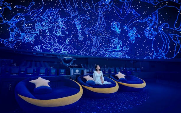 Tourists seated under a starry sky projection at a planetarium.