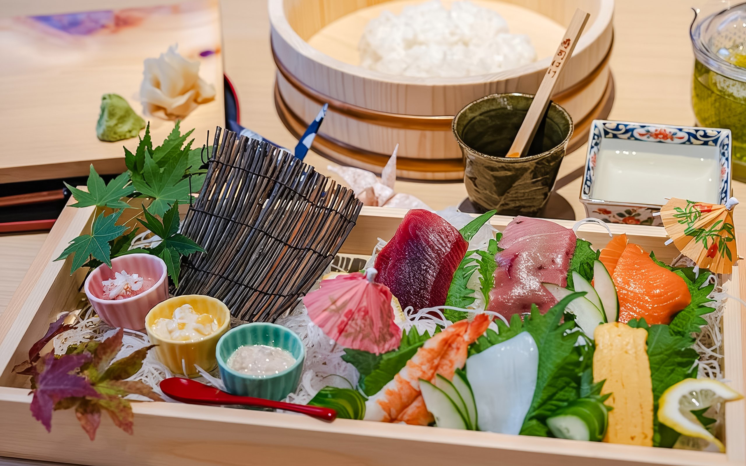 Sushi platter with assorted sashimi, garnishes, and dipping sauces in a wooden box.