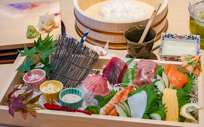 Sushi platter with assorted sashimi, garnishes, and dipping sauces in a wooden box.