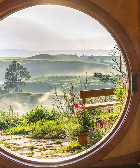 View from Hobbiton house window overlooking lush green hills in New Zealand.