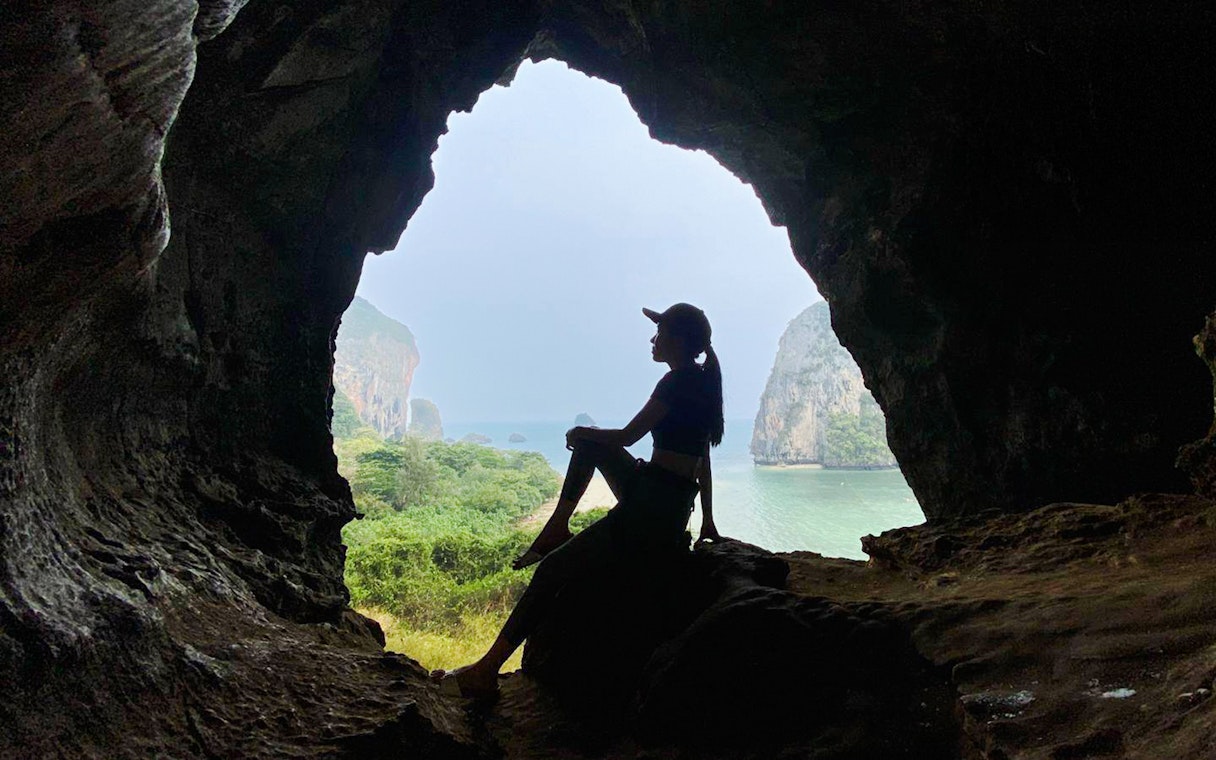 Silhouette of a tourist sitting in a cave at Railay Beach, Krabi, overlooking the sea.