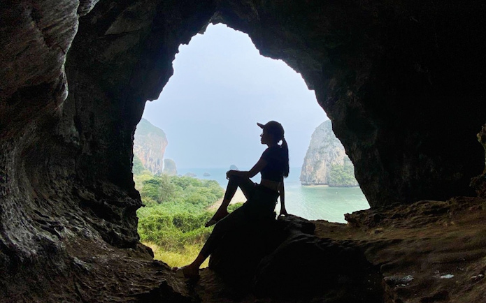 Silhouette of a tourist sitting in a cave at Railay Beach, Krabi, overlooking the sea.