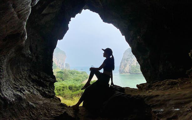 Silhouette of a tourist sitting in a cave at Railay Beach, Krabi, overlooking the sea.