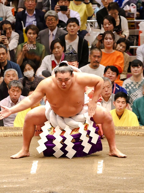 Sumo wrestler performing pre-match ritual in Tokyo ring.