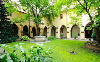 Courtyard of the Minorite Monastery of St. James in Prague with arches and greenery.
