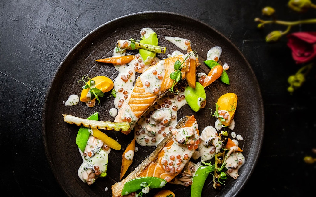 Salmon dish with vegetables and sauce at CÉ LA VI Dubai, featuring Burj Khalifa views.