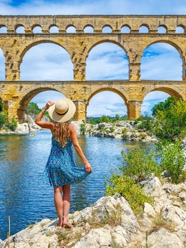 Pont du Gard aqueduct over Gardon River, Provence, with visitor and lush greenery.