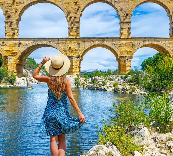 Pont du Gard aqueduct over Gardon River, Provence, with visitor and lush greenery.