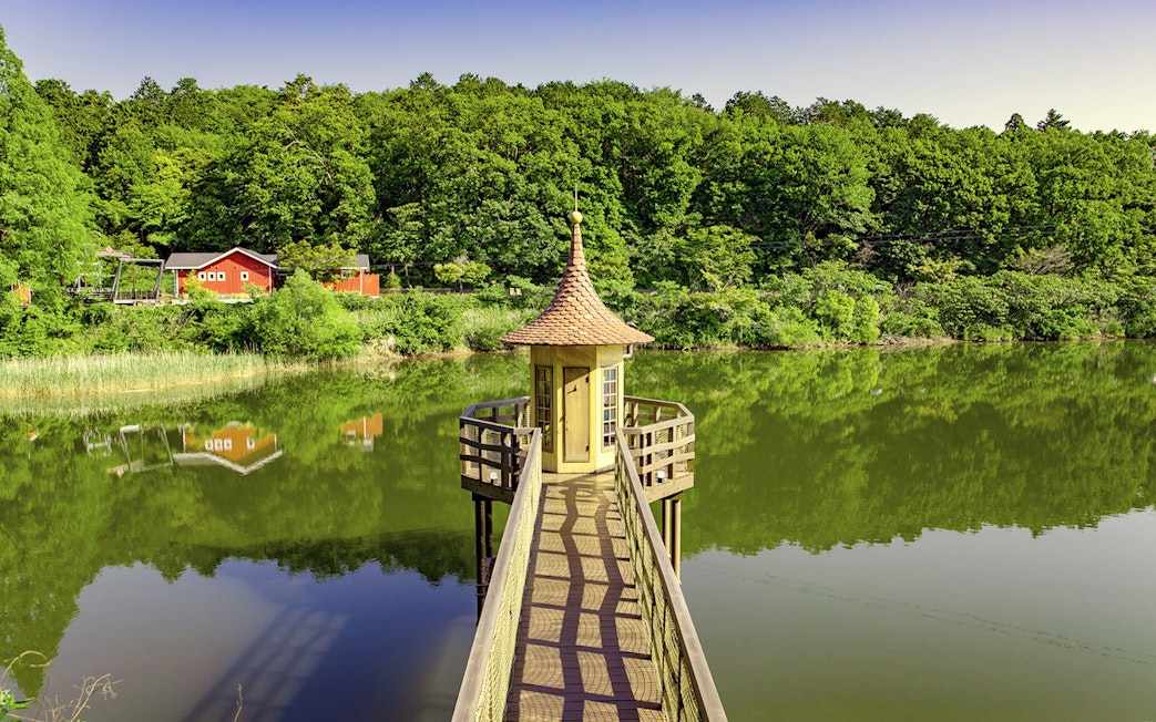 Pathway leading to a small tower over a lake at Moominvalley Park, surrounded by lush greenery.