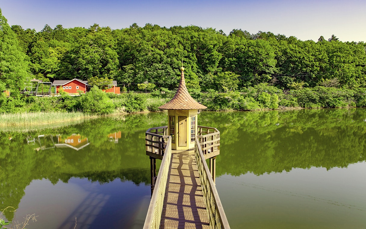 Pathway leading to a small tower over a lake at Moominvalley Park, surrounded by lush greenery.