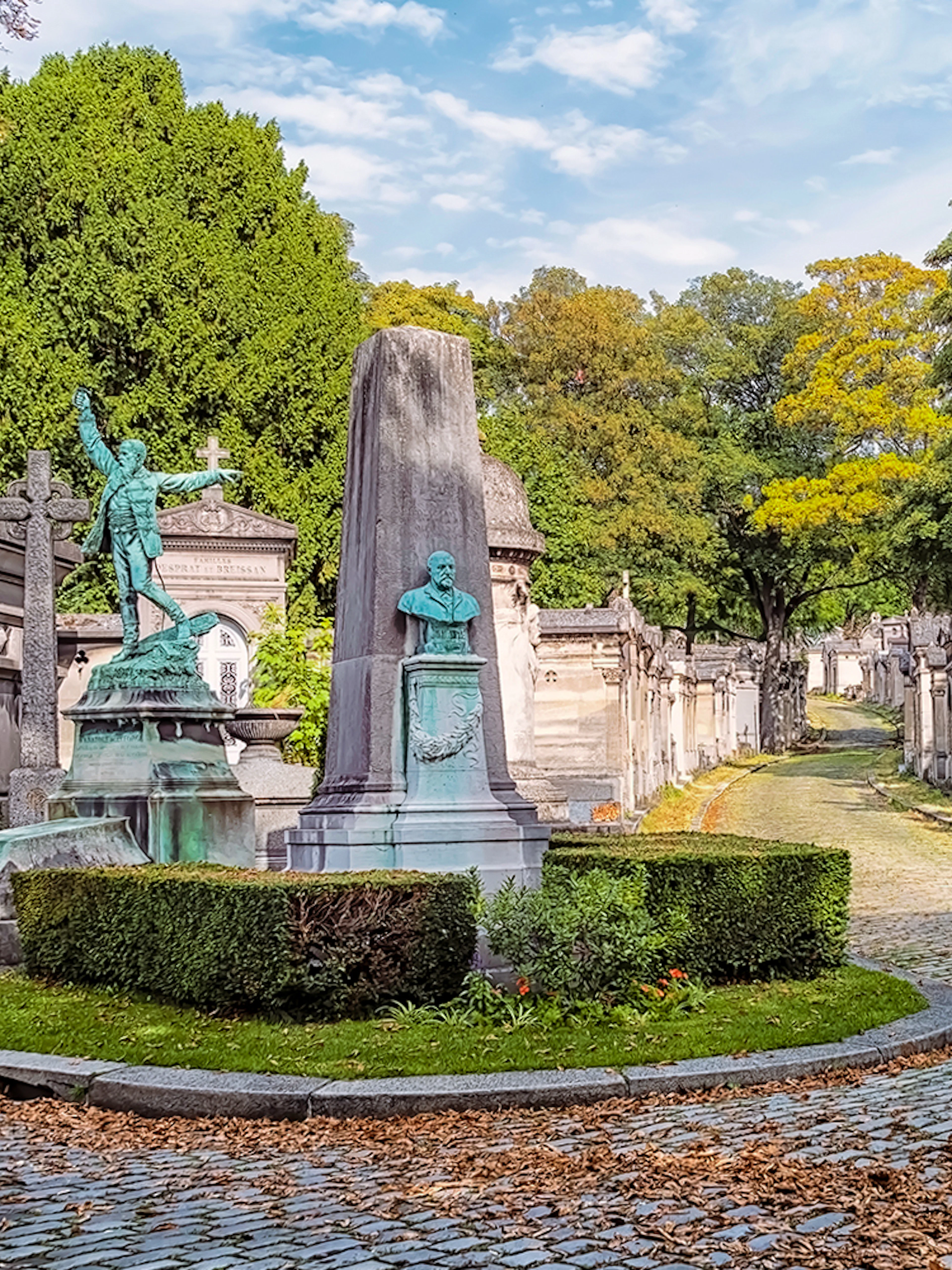 Père Lachaise Cemetery path with ornate tombs and statues, Paris.