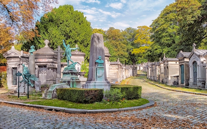 Père Lachaise Cemetery path with ornate tombs and statues, Paris.