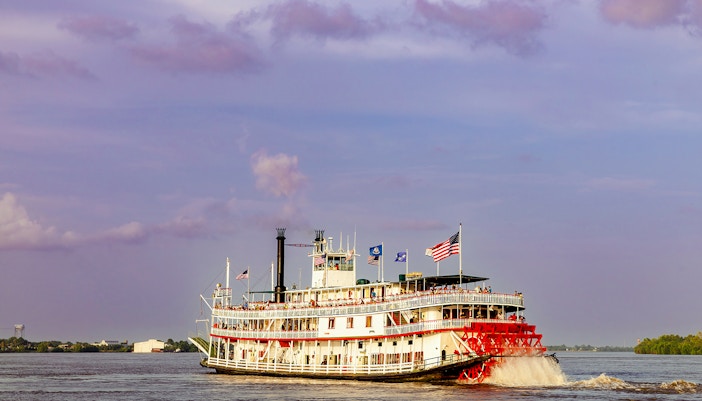 Steamboat Natchez cruising on the Mississippi River with New Orleans skyline in the background.